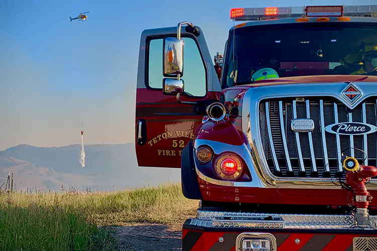A helicopter dumps water behind a fire truck in Teton Village, WY.